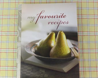 May include: A cookbook titled "my favourite recipes" with a cover image of two pears in a bowl. The pears are yellow-green and sit on top of an open book. The background is a yellow plaid tablecloth.