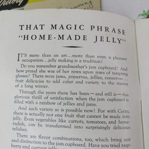 May include: Open book page with the title "THAT MAGIC PHRASE 'HOME-MADE JELLY'" in bold, black font. The text discusses jelly making as a tradition, mentioning jams, preserves, and fruit delicacies. The page is slightly yellowed.