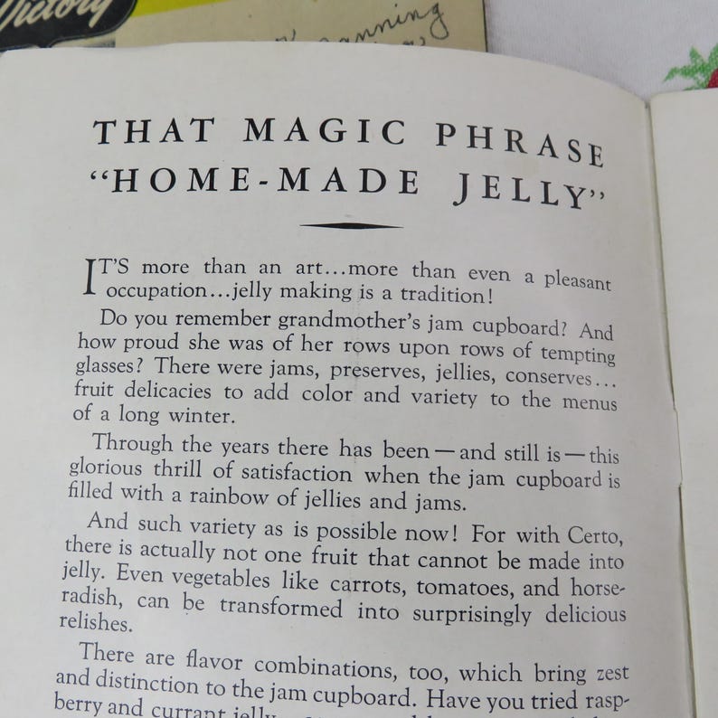 May include: Open book page with the title "THAT MAGIC PHRASE 'HOME-MADE JELLY'" in bold, black font. The text discusses jelly making as a tradition, mentioning jams, preserves, and fruit delicacies. The page is slightly yellowed.