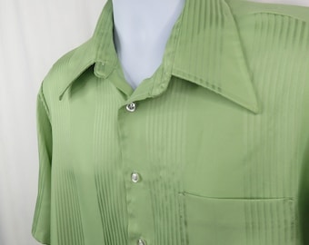 May include: A light green short-sleeve shirt with vertical striped texture. The shirt has a wide collar, a chest pocket, and three visible clear buttons. The shirt is displayed on a white mannequin.