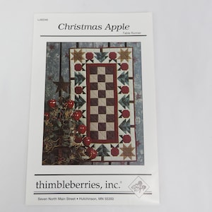 May include: A printed pattern for a Christmas Apple table runner. The design features a central checkerboard pattern, surrounded by Christmas trees, apples, and stars. The text "Christmas Apple" and "thimbleberries, inc." are visible.