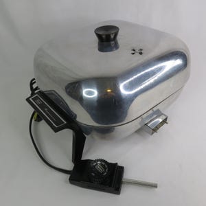 May include: A vintage electric countertop appliance with a shiny, silver-colored exterior. It has a black knob on top and a black control panel with the Sears brand name. The appliance has a rectangular shape with rounded edges.