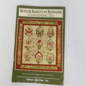 May include: A book cover titled "BUDS & BASKETS IN REDWORK" by Marge Wooters. The cover features a quilt pattern with floral designs in red, green, and cream colors. The pattern includes piecing, applique, and Redwork techniques. The publisher is Indygo Junction, Inc.