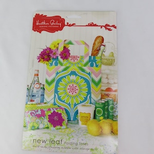 May include: A package for "New Leaf Folding Totes" sewing patterns by Heather Bailey. The tote bag design features a turquoise and lime green floral pattern. The image includes a variety of groceries and flowers.