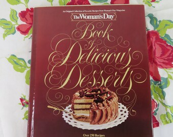 May include: A cookbook titled "The Woman's Day Book of Delicious Desserts" with a maroon cover and gold lettering. The cover features a chocolate cake with a slice cut out. The book is edited by Julie Houston and contains over 250 recipes.