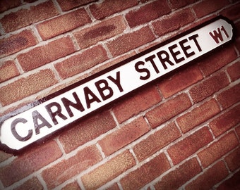 May include: A white sign with black lettering on a brick wall reads "Carnaby Street W1".