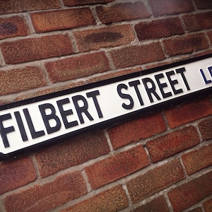 Könnte beinhalten: Ein weißes und schwarzes Straßenschild mit dem Text "FILBERT STREET LE2" an einer Backsteinmauer.