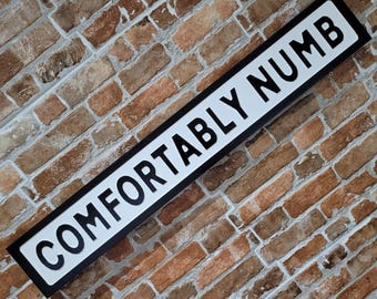 Placa decorativa personalizada "Comfortably Numb" com letras em relevo e efeito de ferro fundido, perfeita para ambientes internos.
