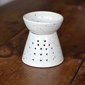 May include: White ceramic essential oil diffuser with a speckled finish. The diffuser has a bowl on top and a perforated base.