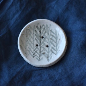 May include: A white ceramic soap dish with a grey and white leaf pattern. The dish has three drainage holes.
