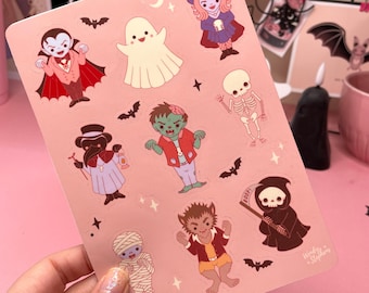 Könnte beinhalten: Ein Bogen mit Halloween-Stickern mit Cartoon-Illustrationen eines Vampirs, Geistes, einer Hexe, eines Zombies, eines Skeletts, eines Pestdoktors, einer Mumie, eines Werwolfs und des Sensenmanns. Die Aufkleber sind auf rosa Hintergrund.