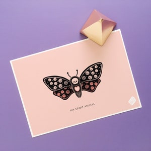 May include: A pink and white card with a black and white butterfly illustration. The butterfly has a heart in the center and is surrounded by skulls. The text "My Spirit Animal" is printed below the butterfly.