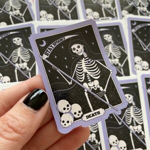 May include: A purple and black tarot card with a skeleton holding a scythe. The card says "Stay Spooky" and "Death".
