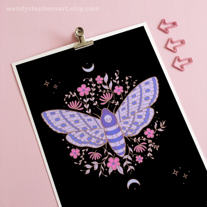 May include: A black background with a purple and blue moth with a skull on its head surrounded by pink and white flowers and gold leaves. There are gold crescent moons and stars in the corners.
