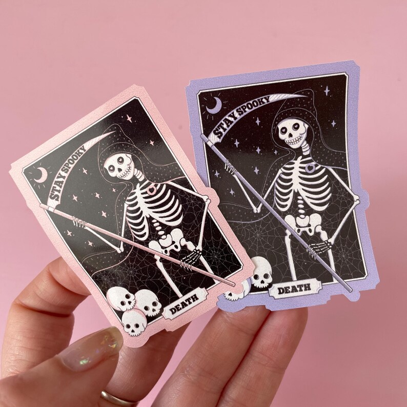 May include: Two pink and purple stickers with a skeleton wearing a hooded robe and holding a scythe. The stickers have a black background with white stars and the text "Stay Spooky" and "Death".