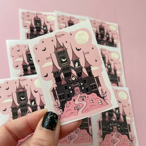May include: A set of eight pink and black stickers featuring a spooky, gothic-style castle with a clock tower and bats. The castle is surrounded by a graveyard with tombstones and a path leading to the front door. The stickers are perfect for adding a touch of spooky charm to your planner, laptop, or water bottle.