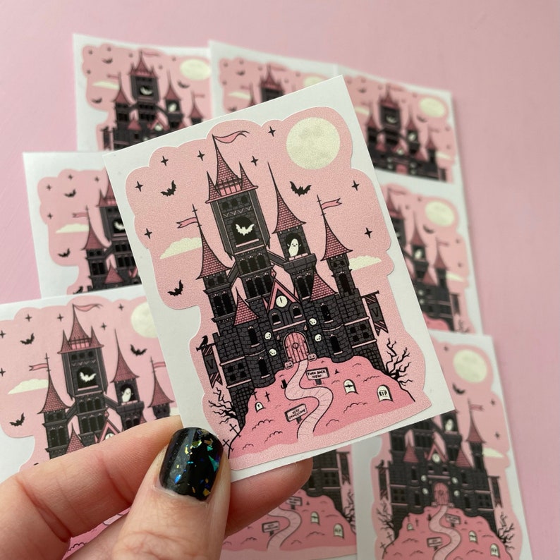 May include: A set of eight pink and black stickers featuring a spooky, gothic-style castle with a clock tower and bats. The castle is surrounded by a graveyard with tombstones and a path leading to the front door. The stickers are perfect for adding a touch of spooky charm to your planner, laptop, or water bottle.