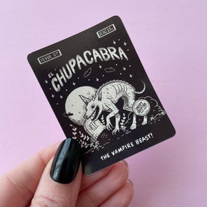 May include: Black and white illustration of a creature called "El Chupacabra" on a black card with white text. The text reads "Issue 07, El Chupacabra, The Vampire Beast!" and "Creepy Cryptids".