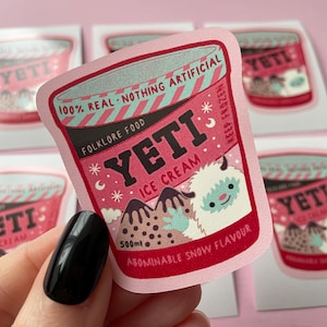 May include: Pink sticker with a cartoon illustration of a Yeti holding a cup of ice cream. The ice cream container is labeled "Yeti Ice Cream" and "Abominable Snow Flavor". The sticker is 500 ml.