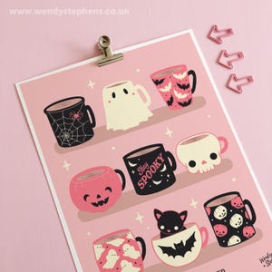 Op de afbeelding: Een roze poster met illustraties van Halloween-mokken. Ontwerpen omvatten een spinnenweb, een spook, vleermuizen, een schedel, een pompoen en een zwarte kat. De tekst "Stay Spooky" staat op een mok. De website www.wendystephens.co.uk staat bovenaan.