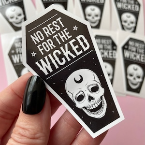 May include: Black and white coffin-shaped sticker with the text "NO REST FOR THE WICKED" and a skull illustration. The skull has a crescent moon above it. Additional stickers are visible in the background.
