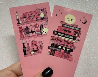 May include: Two pink bookmarks with a Halloween theme. The bookmark on the left features a bookshelf with potions, spells, and a skull. The bookmark on the right features a stack of books with titles like "Coven", "Poisons & Potions", and "Magick Spells".
