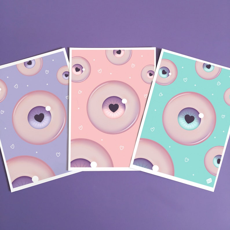 May include: Three different colored cards with a repeating pattern of pink eyes with a purple heart in the center. The cards are light purple, light pink, and light blue.