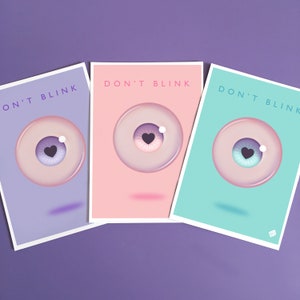May include: Three pastel colored cards with the text "Don't Blink" and a cartoon eye with a heart in the pupil. The cards are purple, pink, and turquoise.