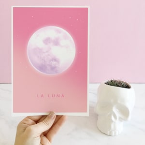 May include: A pink and purple illustration of a full moon with the text "LA LUNA" printed below. The image is printed on a white card.