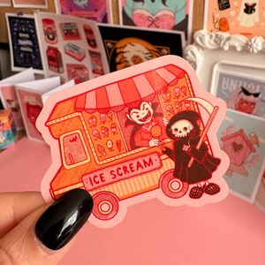 May include: A die-cut sticker featuring an orange and red ice cream truck with a striped awning. A vampire serves a scoop of ice cream to a hooded skeleton figure holding a scythe. The truck has the text ICE SCREAM printed on the side panel.