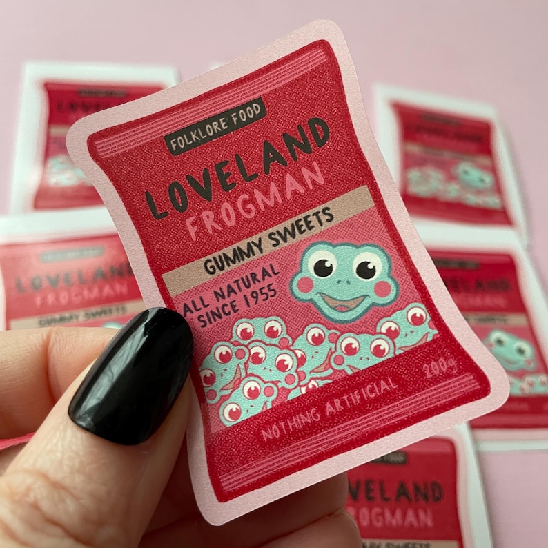 May include: A pink and red sticker with the text "LOVELAND FROGMAN GUMMY SWEETS ALL NATURAL SINCE 1955 NOTHING ARTIFICIAL 200g" and a cartoon frog with a big smile.
