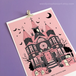 May include: A pink and black illustration of a spooky haunted house with a crescent moon, bats, and a ghost in the attic. The house has a spiderweb on the front and a sign that says "Spooky Drive". The text at the bottom reads "Sweet Haunted Home".