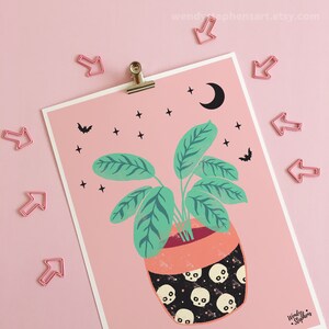 May include: A pink background with a green plant in a black and white skull patterned pot. The plant has large green leaves and is surrounded by small white stars and black bats. A crescent moon is in the top right corner.