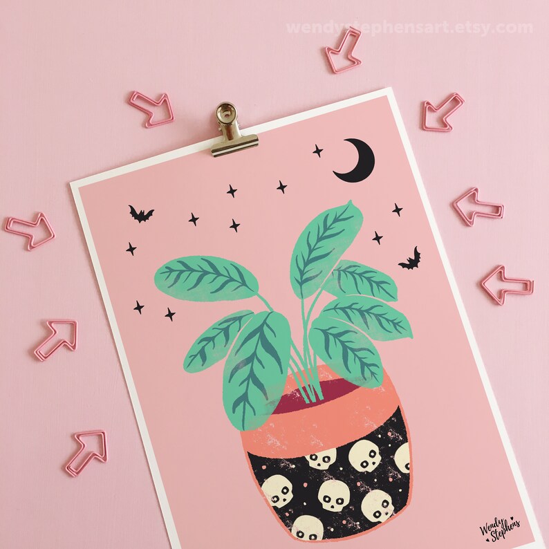 May include: A pink background with a green plant in a black and white skull patterned pot. The plant has large green leaves and is surrounded by small white stars and black bats. A crescent moon is in the top right corner.