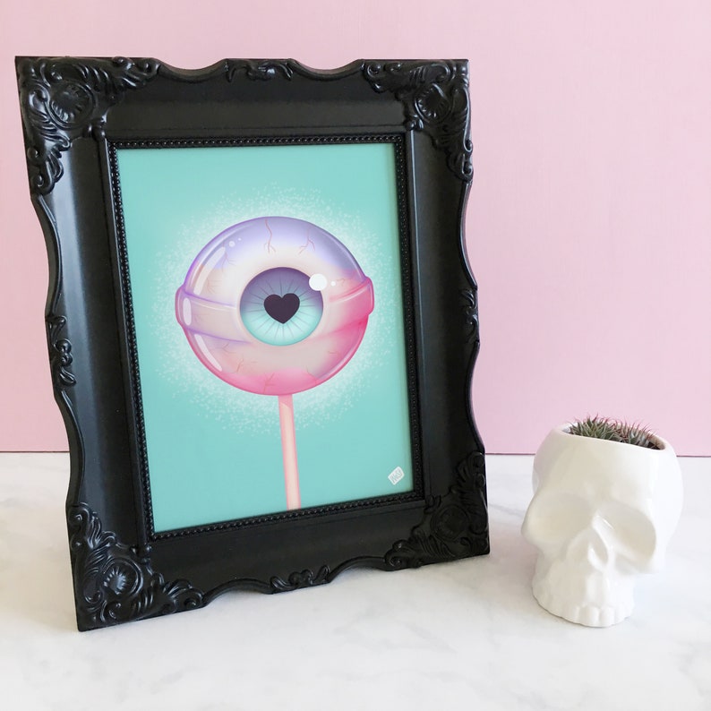May include: A framed print of a colorful eyeball lollipop with a heart-shaped pupil on a turquoise background.
