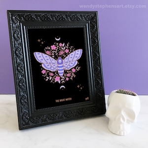 May include: A framed print of a moth with pink and purple wings, surrounded by flowers and a crescent moon. The print is on black paper and has the text "The Night Watch" at the bottom.