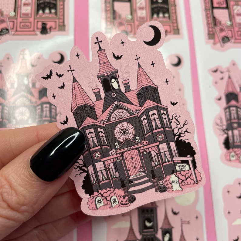 May include: Pink and black sticker of a spooky house with a spiderweb, bats, and a ghost. The house has a sign that says "Spooky Drive" and a tombstone that says "RIP".