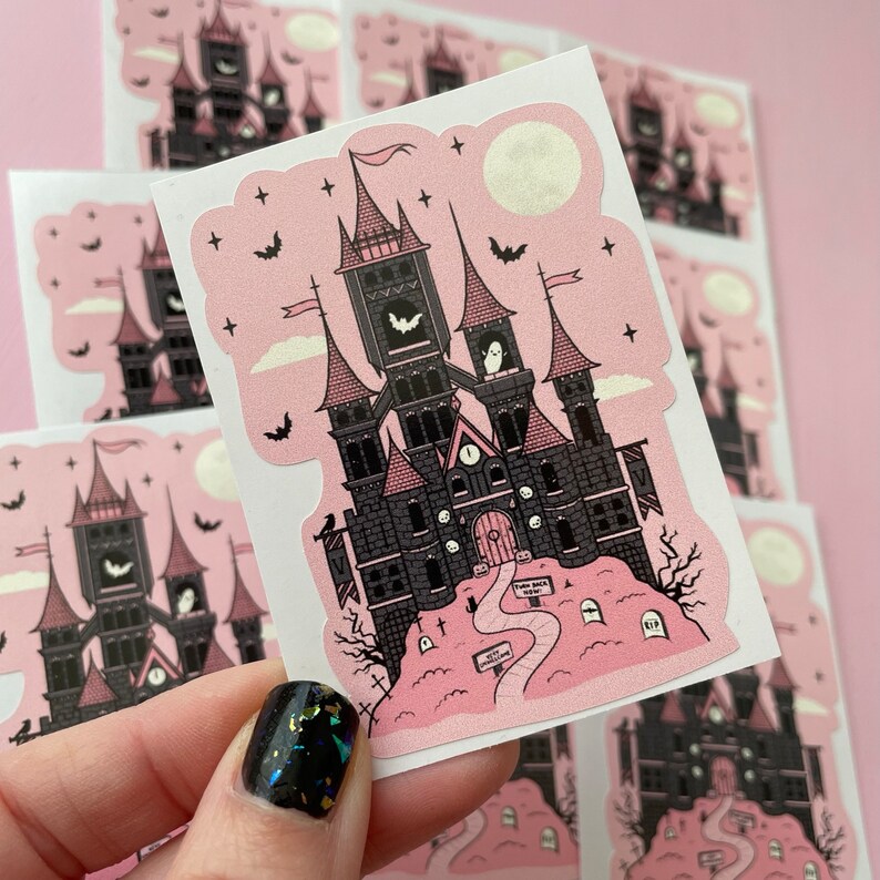 May include: Pink and black sticker featuring a spooky gothic castle with a clock tower, bats, and ghosts. The castle is surrounded by a graveyard with tombstones and a path leading to the front door. The sticker has a pink background and white clouds.