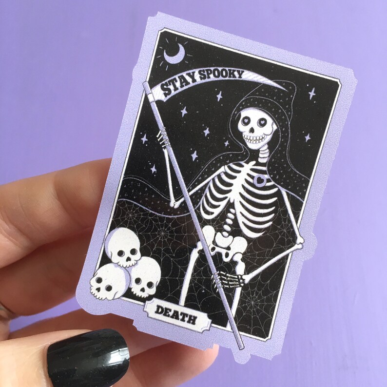 May include: A purple and black illustrated card with a skeleton holding a scythe. The card says "Stay Spooky" and "Death".