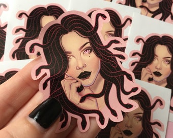 May include: A sticker featuring a pink background with a black and white illustration of a woman with snakes for hair. The woman has pink eyes and is looking at the viewer. The snakes are curled around her head and neck.