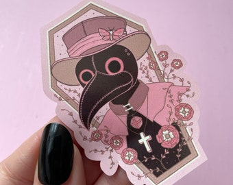 May include: A pink and black plague doctor sticker with a pink hat and a cross on a chain. The sticker is surrounded by pink flowers and vines.