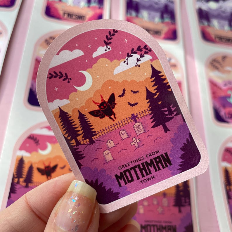 K&ouml;nnte beinhalten: Ein rosa Aufkleber mit einer fantasievollen Illustration eines Mothman, der nachts &uuml;ber einen Friedhof fliegt. Der Aufkleber hat einen rosa Rand und den Text "Greetings from Mothman Town" unten.