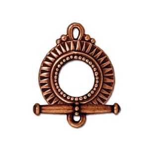 May include: A copper-colored toggle clasp with a circular design. The clasp features a central ring, a horizontal bar, and a decorative top loop. The circular portion has a sunburst pattern and a beaded inner circle. The toggle clasp is designed for jewelry making.
