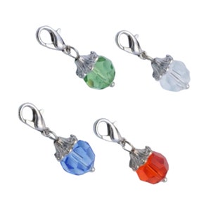 May include: Four colorful charms with lobster clasps. Each charm features a faceted, jewel-toned bead in green, white, blue, and red. The beads are attached to a decorative silver-colored metal base and clasp.