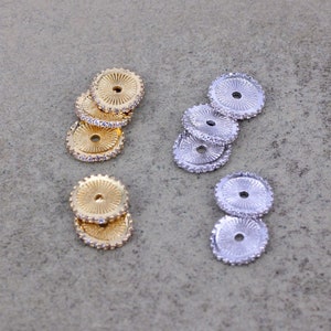 May include: Two sets of round, decorative metal beads with a raised center and a clear rhinestone border. One set is gold and the other is silver.