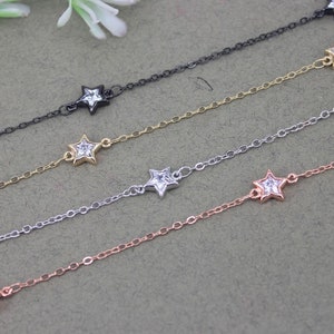 May include: Four delicate silver chains with star-shaped charms, each featuring a clear crystal center. The chains are layered on a gray textured surface.