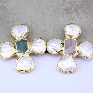 May include: Two cross-shaped pendants with gold-toned metal frames. Each pendant features four white iridescent shell petals surrounding a central stone. The left pendant has a green stone, and the right pendant has a mauve-colored stone.