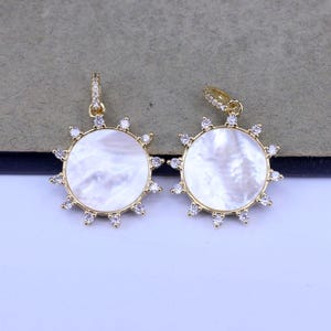 May include: Two gold-tone pendants with a white mother-of-pearl center and clear crystal accents around the edge.