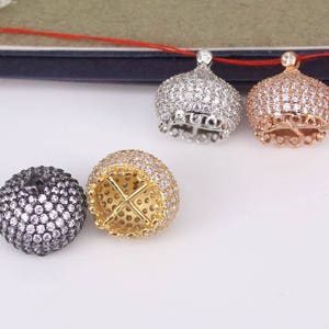 Könnte beinhalten: Vier silberne, goldene und schwarze Metallperlenkappen mit klaren Kristallverzierungen. Die Kappen sind rund und haben ein dekoratives Design.