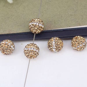 May include: Five gold-toned round beads with clear rhinestones. The beads are strung on a silver wire.